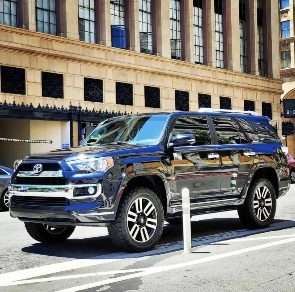 A black Toyota 4Runner SUV is parked on a city street in front of a tall building with large windows.