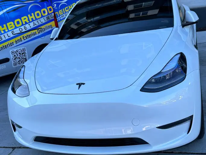 A white Tesla Model 3 parked in front of a van advertising Neighborhood Mobile Detailing services.